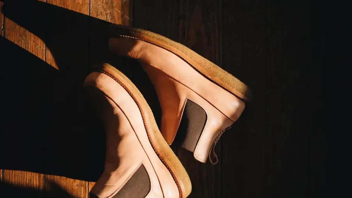 Bottines claires en cuir posées sur un parquet, éclairées par le soleil