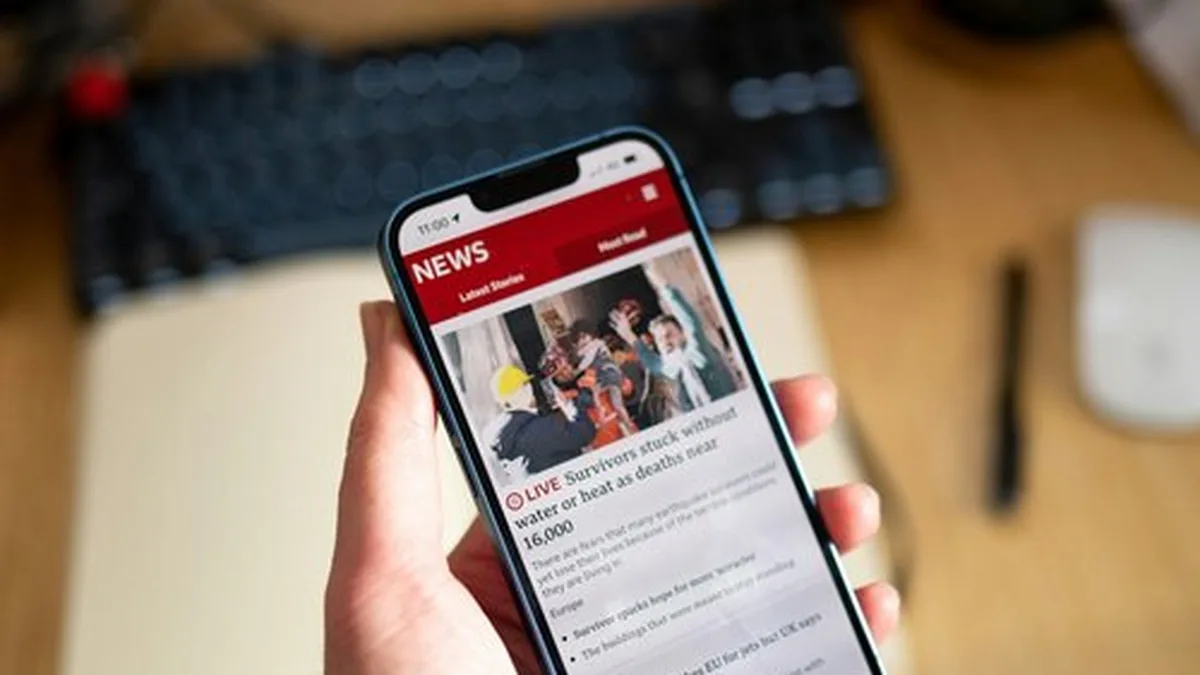 Une main tenant un smartphone affichant des articles d&rsquo;actualité