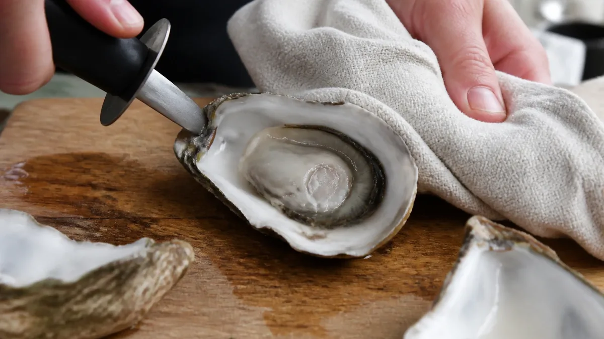 Ouverture d&rsquo;une huître au couteau, la main protégée par un torchon