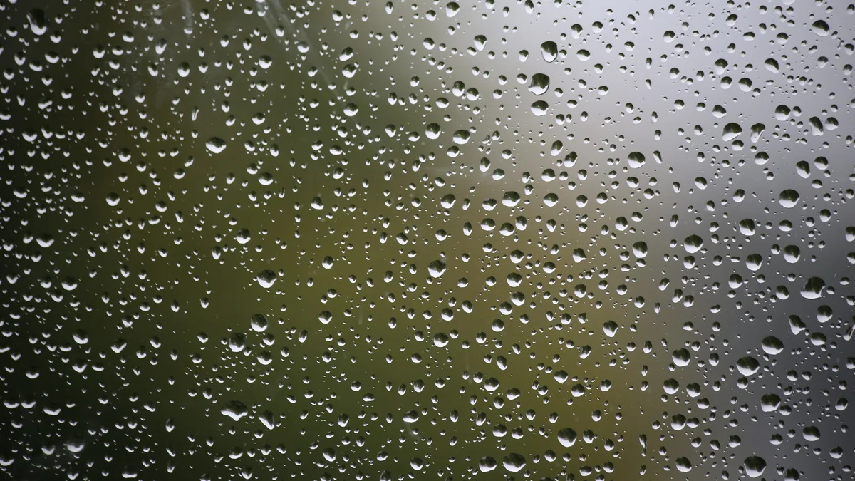 De la pluie ruisselle sur une vitre, des feuilles d&rsquo;automne floues en arrière-plan