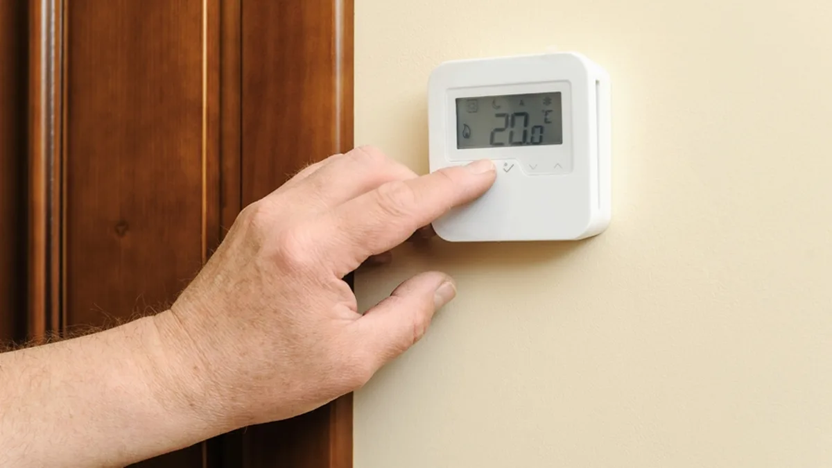 Une main règle un thermostat mural affichant 20 degrés