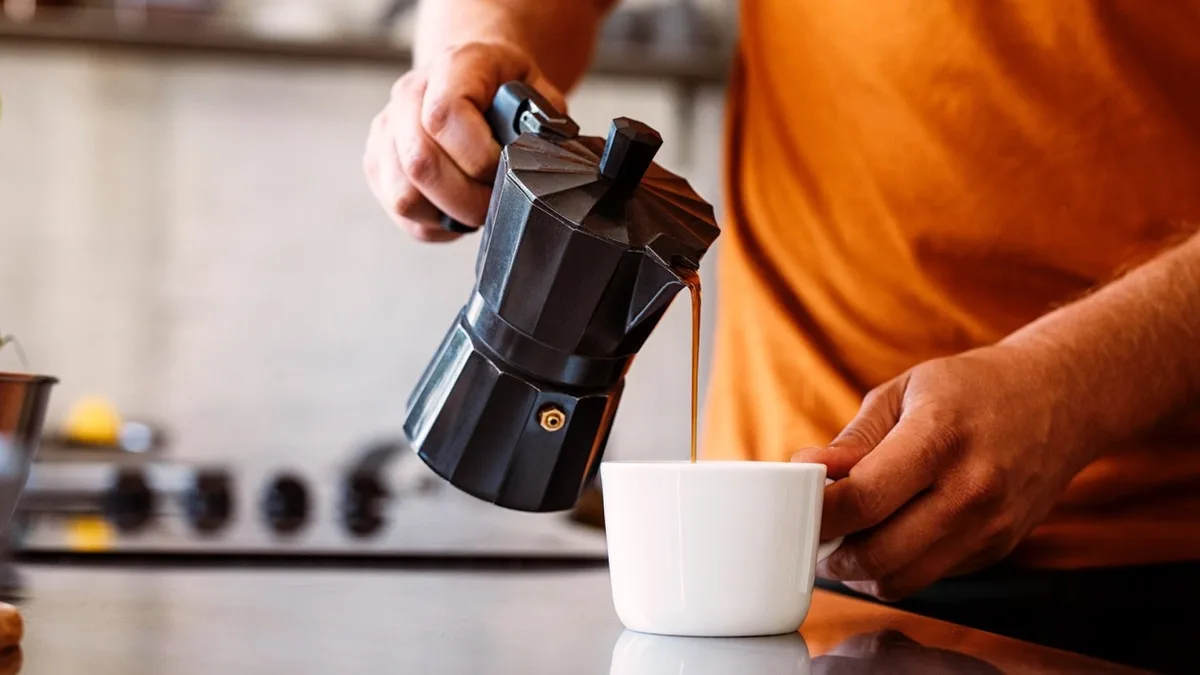 Une personne verse le café d&rsquo;une cafetière italienne dans une tasse blanche